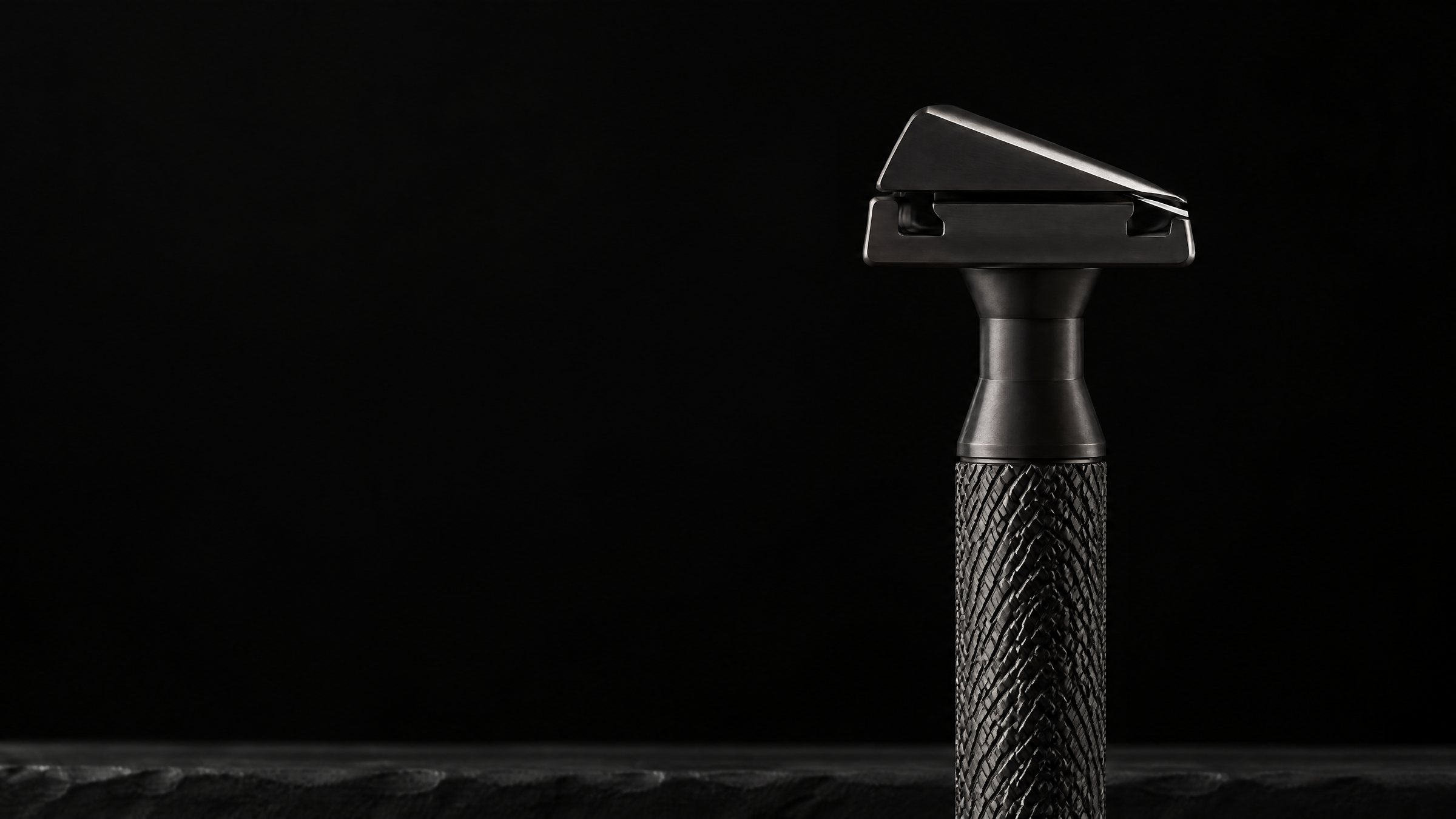 The graphite razor head seen from its short end, the top cap sloping at 30 degrees over the blade edge